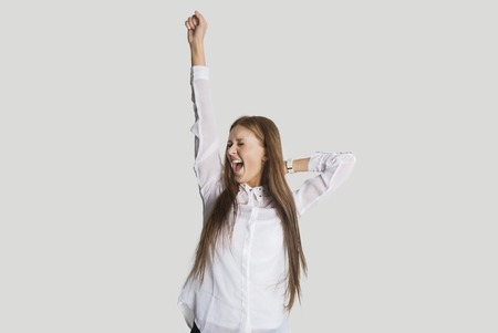 Excited woman with arm raised screaming against white backgroundの写真素材