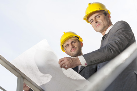 Low angle portrait of confident young businessmen holding blueprint against clear skyの写真素材
