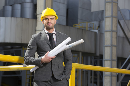 Portrait of confident young businessman holding blueprints outside industryの写真素材