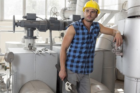 Young labor holding wrench while leaning on industrial machine
