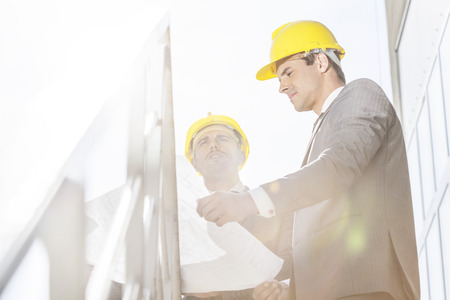 Low angle view of young businessman in hard hats reviewing blueprint on stairway