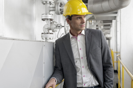 Young male architect in hard hat looking away at industry