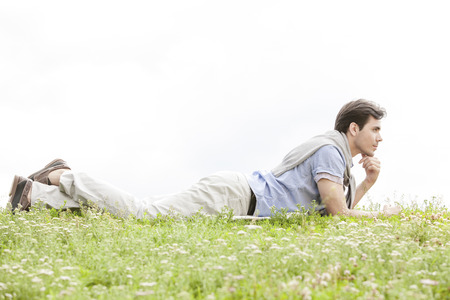 Full length of thoughtful young man lying on grass against clear skyの写真素材