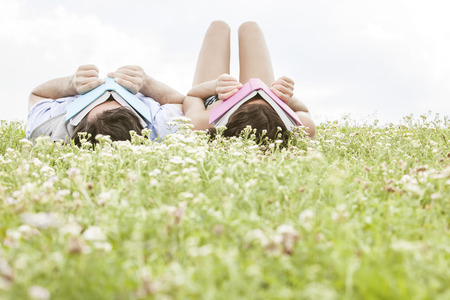 Relaxed young couple covering faces with books while lying on grassの写真素材