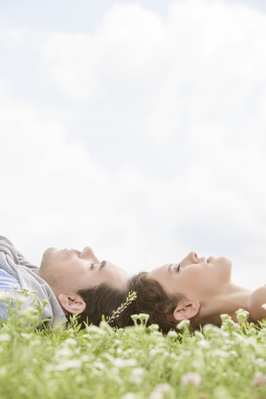 Side view of young couple sleeping on grass against skyの写真素材