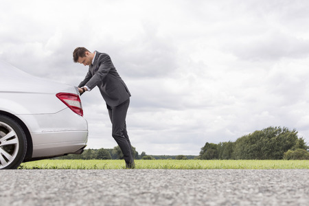 Side view of tired young businessman pushing car at countrysideの写真素材