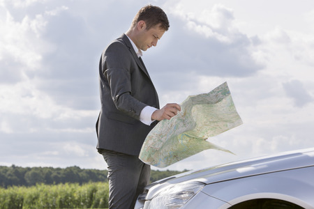 Side view of young businessman reading map by car at countrysideの写真素材