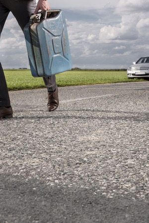 Low section of businessman carrying gasoline can with broken car in background at countrysideの写真素材