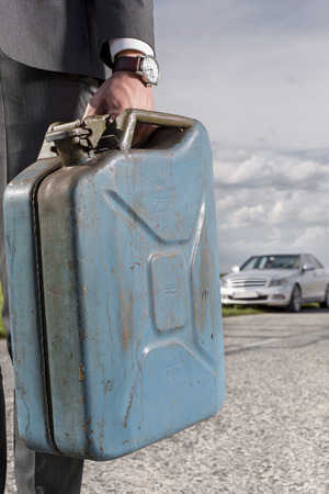Low section of young businessman carrying gasoline can with broken car in background at countrysideの写真素材