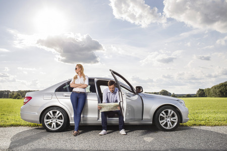 Full length of young woman looking away while man reading map in car at countrysideの写真素材