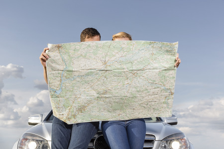 Couple reading map while leaning on car hood during road tripの写真素材