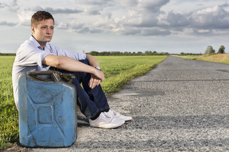Full length of young man with empty gas can sitting by roadの写真素材