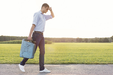 Full length of tired young man with gas can walking on rural roadの写真素材