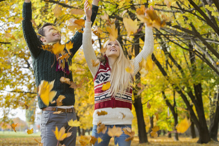Couple enjoying falling autumn leaves in park