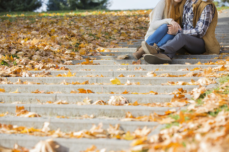 Low section of couple sitting on steps in park during autumnの写真素材