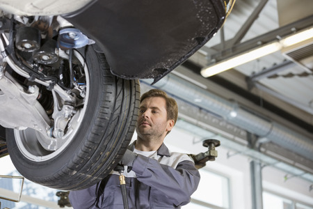 Mid adult technician repairing car's wheel in workshopの写真素材