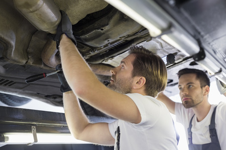 Male repair workers examining car in workshopの写真素材