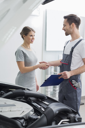 Young repair worker shaking hands with customer in car workshopの写真素材