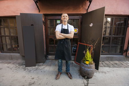 Portrait of confident male salesperson standing arms crossed outside coffee storeの写真素材
