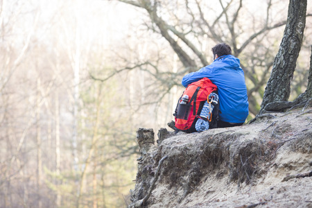 Rear view of hiker with backpack sitting on edge of cliff in forestの写真素材