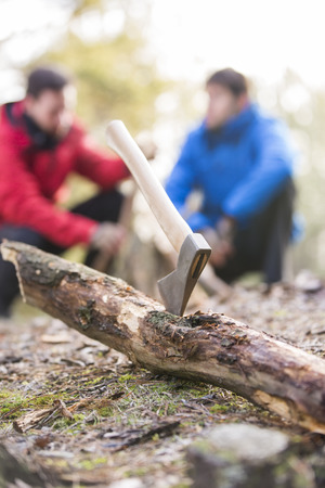 Axe stuck in log with male hikers in background at forestの写真素材