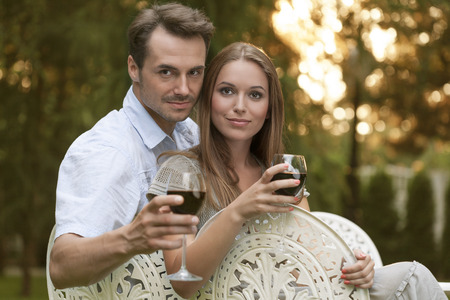 Portrait of young couple having red wine on chairs in parkの写真素材