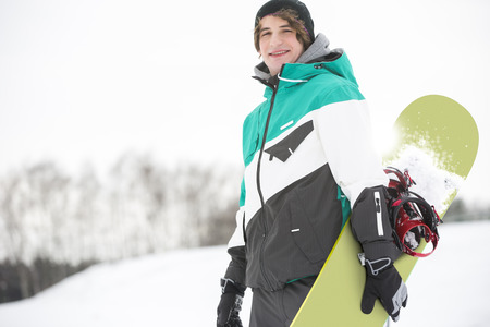 Portrait of handsome young man with snowboard in snowの写真素材