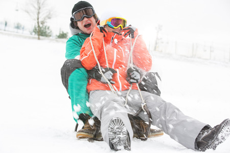Excited young couple sledding in snowの写真素材