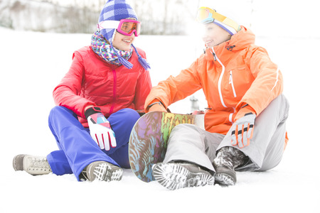 Full length of female friends with snowboard relaxing on snowの写真素材