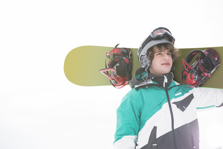 young man carrying snowboard against clear skyの写真素材