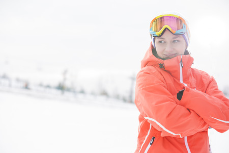 Happy young woman in warm clothing standing arms crossed on snowy fieldの写真素材