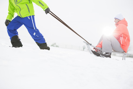 Low section of man giving sled ride to woman in snowの写真素材