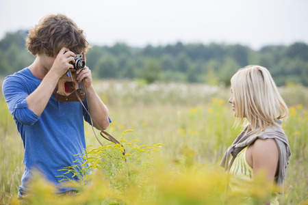 Young man photographing woman in fieldの写真素材
