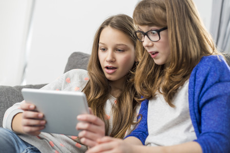 Shocked sisters using digital tablet on sofa at homeの写真素材