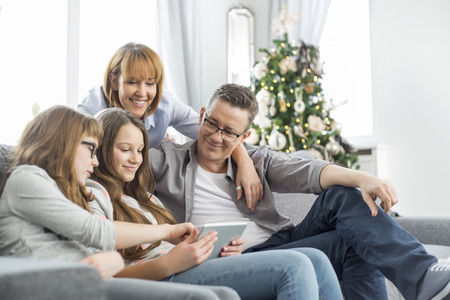 Family using tablet PC on sofa with Christmas tree in backgroundの写真素材