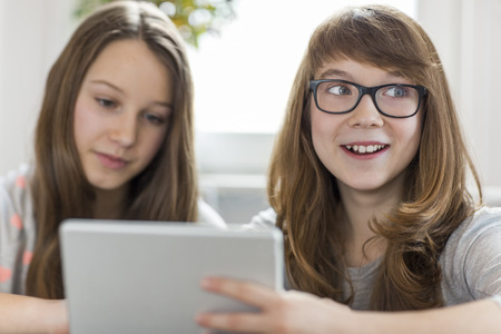 Happy girl with sister using digital tablet at homeの写真素材