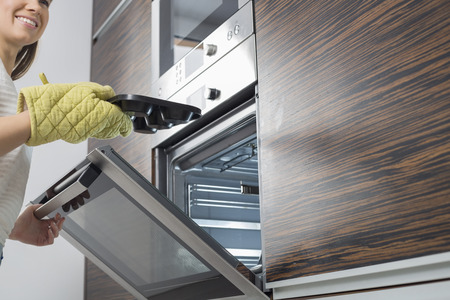 Cropped image of smiling woman removing dish from ovenの写真素材