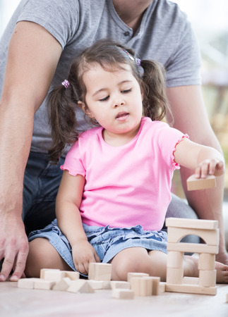 Little girl playing with wooden blocks against father in houseの写真素材