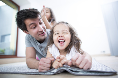 Father looking at cheerful daughter lying on blanket at homeの写真素材