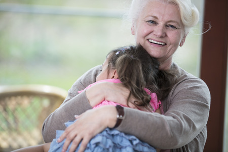 Portrait of happy grandmother hugging granddaughter in houseの写真素材