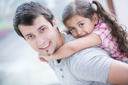 Side view portrait of smiling man piggybacking little daughter at homeの写真素材