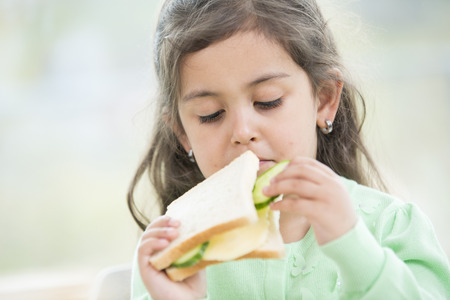 Cute girl eating sandwich at homeの写真素材