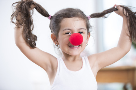 Portrait of playful little girl wearing clown nose holding pigtails at homeの写真素材