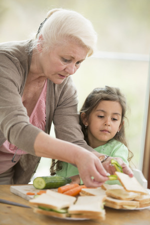 Girl looking at grandmother preparing sandwiches at homeの写真素材