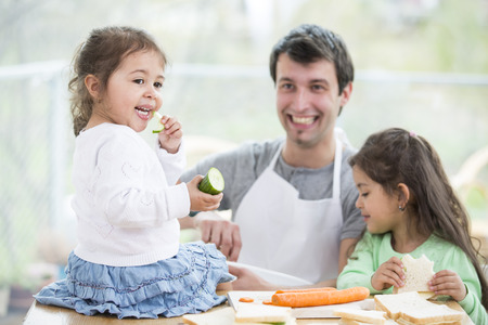 Happy father preparing sandwiches while daughters eating at homeの写真素材