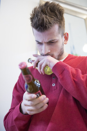 Young man reading label on beer bottle in cafeの写真素材