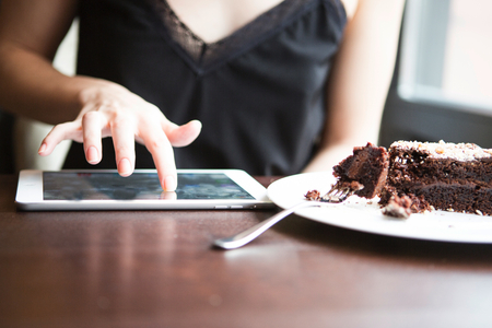 Midsection of woman using tablet PC by pastry in cafeの写真素材