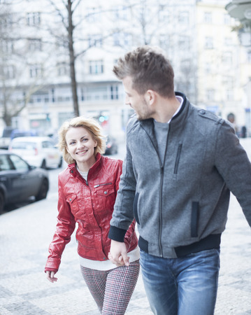 Happy young couple holding hands while walking on city streetの写真素材