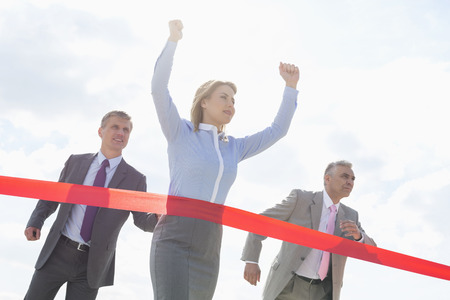 Businesswoman crossing finishing line with colleagues in backgroundの写真素材