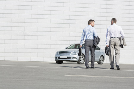 Rear view of businessmen carrying briefcases while walking towards car on streetの写真素材